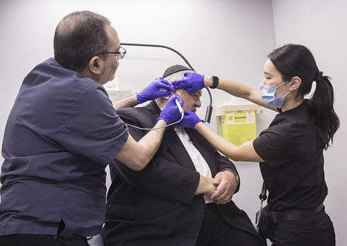Deux médecins prendant la biopsie d’une tumeur cancéreuse derrière l’oreille d’un patient.